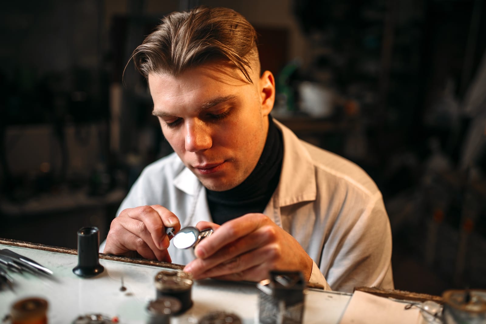 Orologiaio al banco che esamina un orologio da tasca con una lente